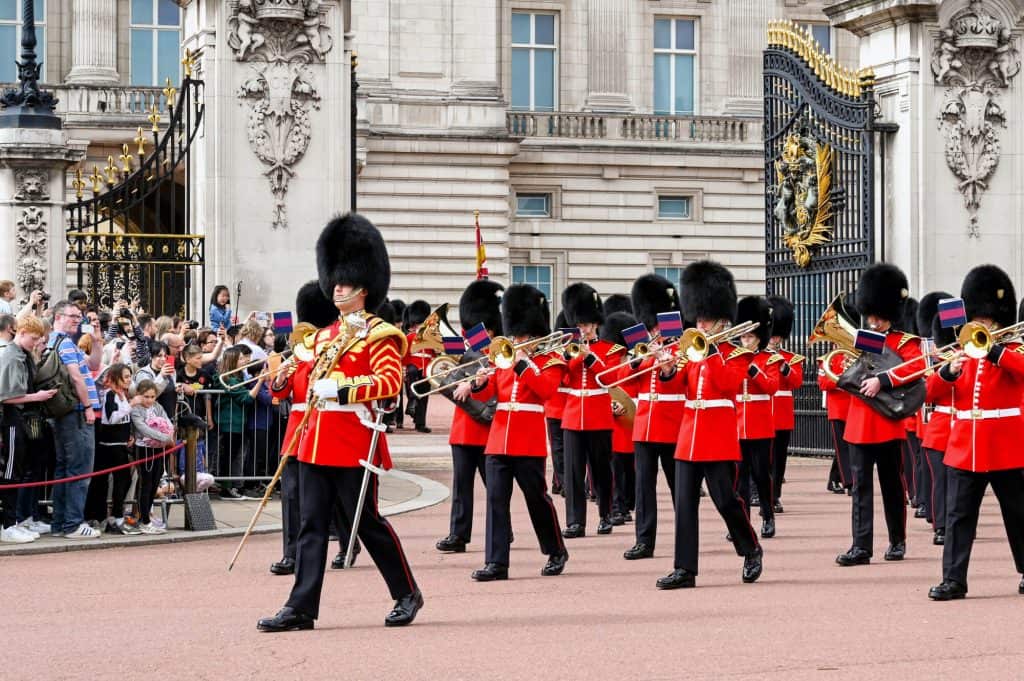 Soldiers in red jackets and bearskin hats marching in front of Buckingham Palace