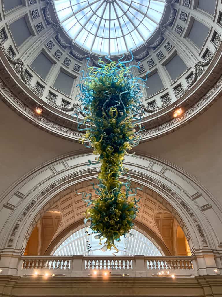 A blue and yellow glass artwork suspended from the ceiling at the V&A museum.