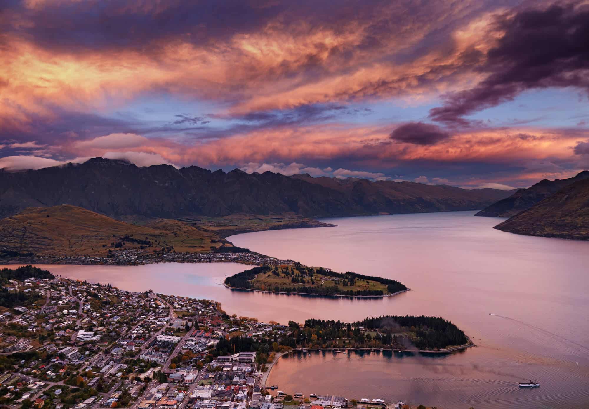 Queenstown New Zealand at sunset, the sky and lake are tinted purple from the sunset
