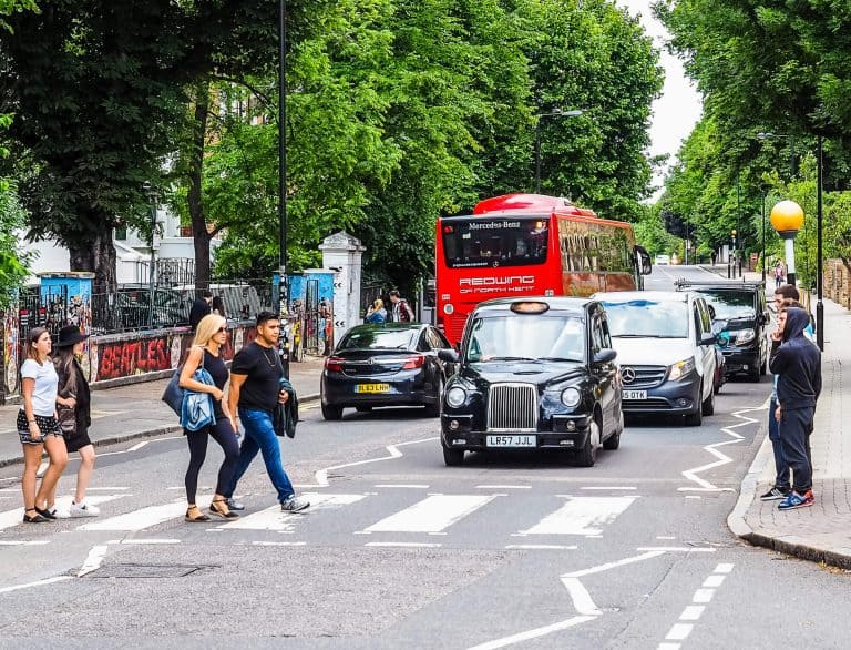 People crossing a London road at a pedestrian crossing with a red bus and black taxi behind them